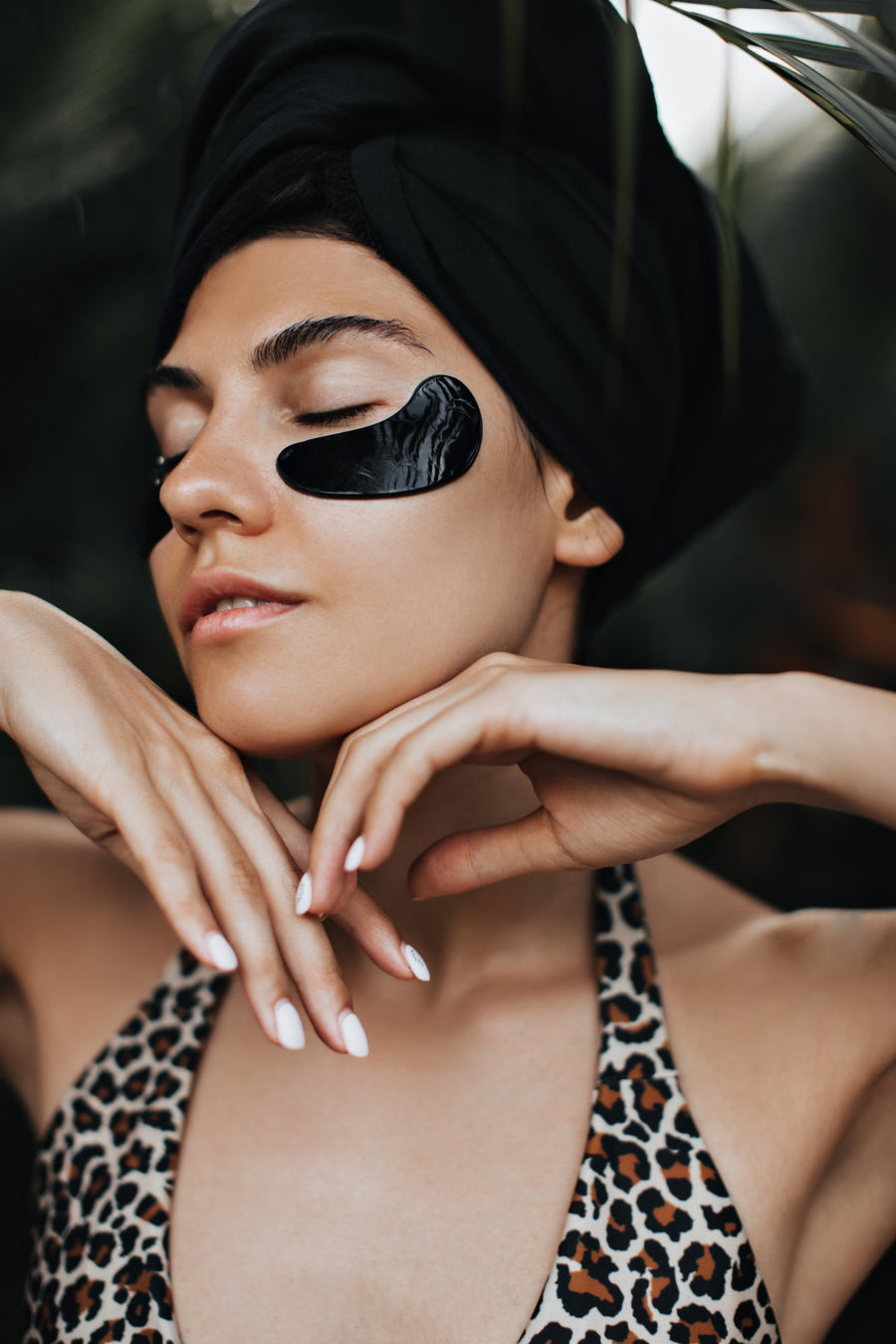 Woman with black eye patches and a leopard print top, surrounded by greenery.