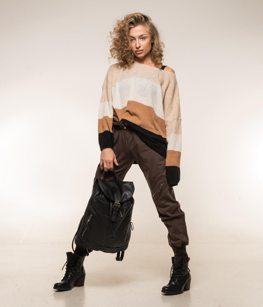Woman wearing a color-blocked sweater and brown pants holding a black bag on a white background